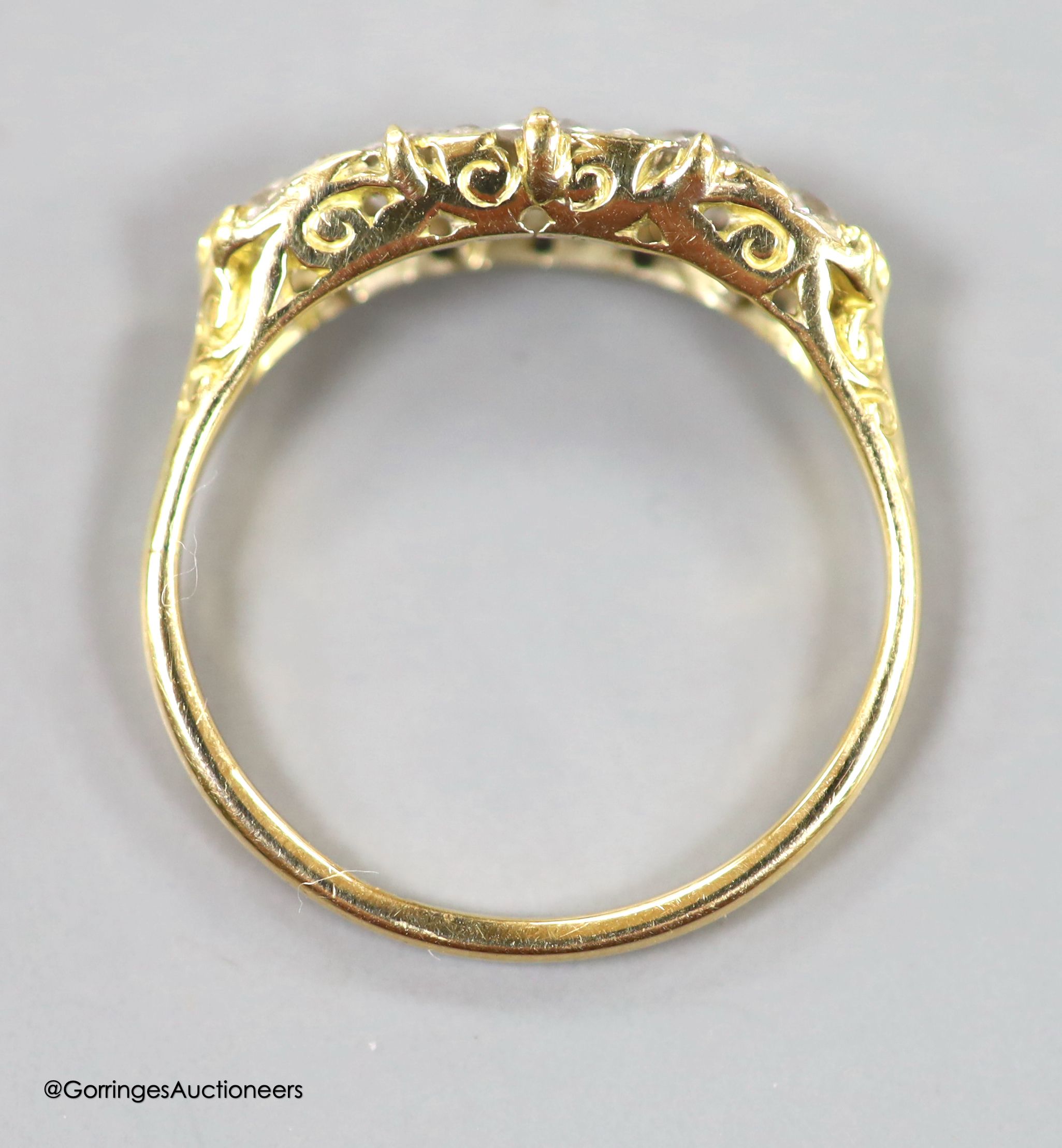 An early 20th century 18ct and graduated five stone diamond set half hoop ring, with diamond chip spacers and carved shoulders, size P, gross weight 2.8 grams